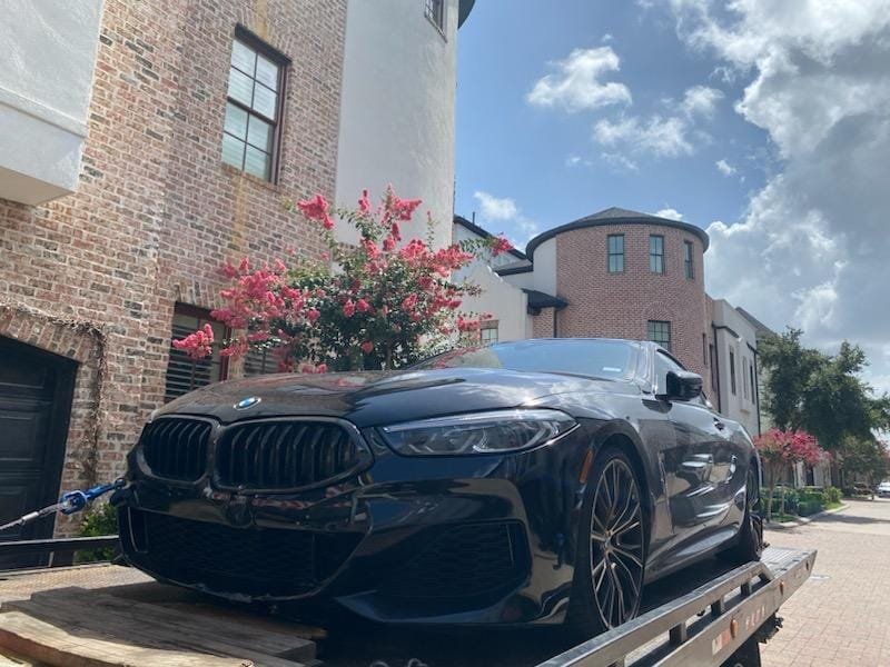 Black BMW on a flatbed beside a building - AA Affordable Towing